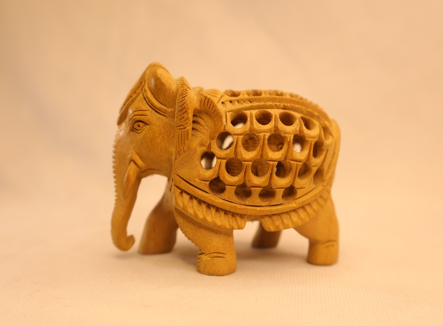 Hand-carved light-wood elephant with intricate jali (lattice) carving, decorative home decor artifact. Hand-carved light-wood elephant with intricate jali (lattice) carving, decorative home decor artifact.