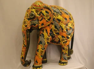 Large hand-painted wooden elephant statue with vibrant yellow, orange and black foliate and animal motifs — decorative Indian folk art sculpture.