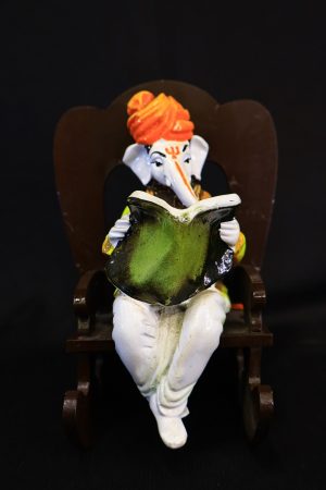 Ganesha (Ganpati) seated in a wooden rocking chair reading a book